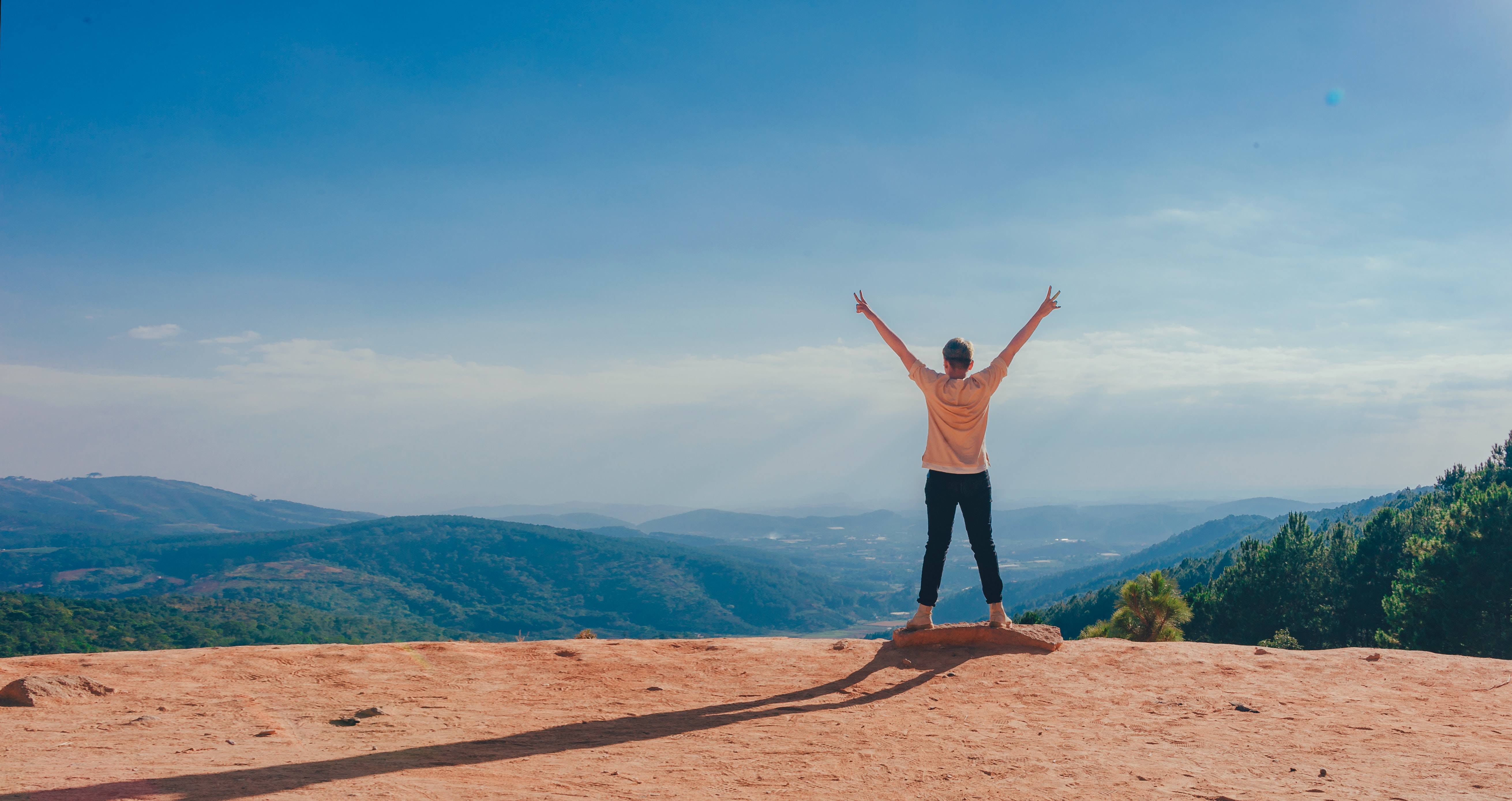 woman standing on cliff edge with arms up