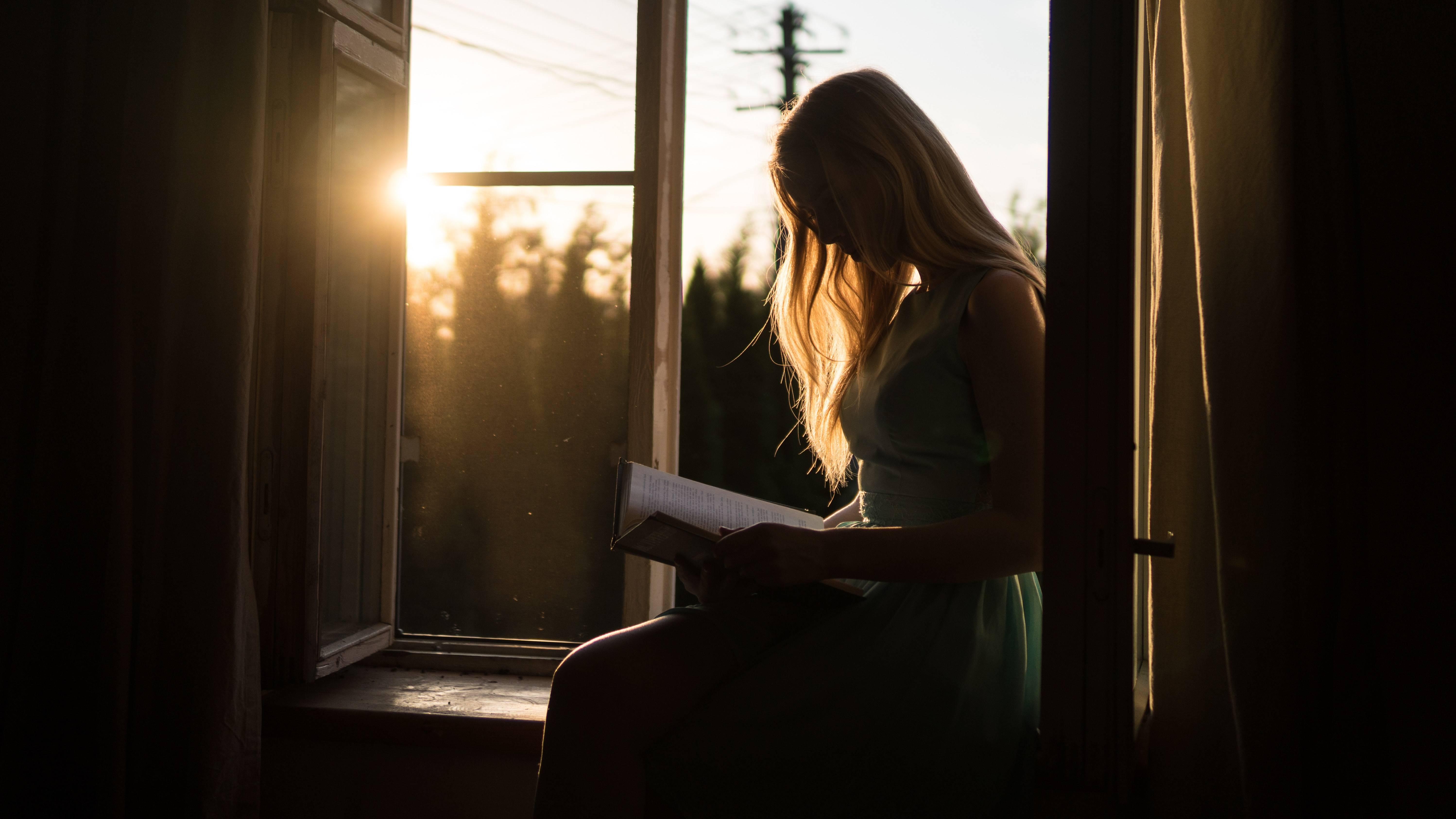 silhouette of a woman reading a book in front of a window