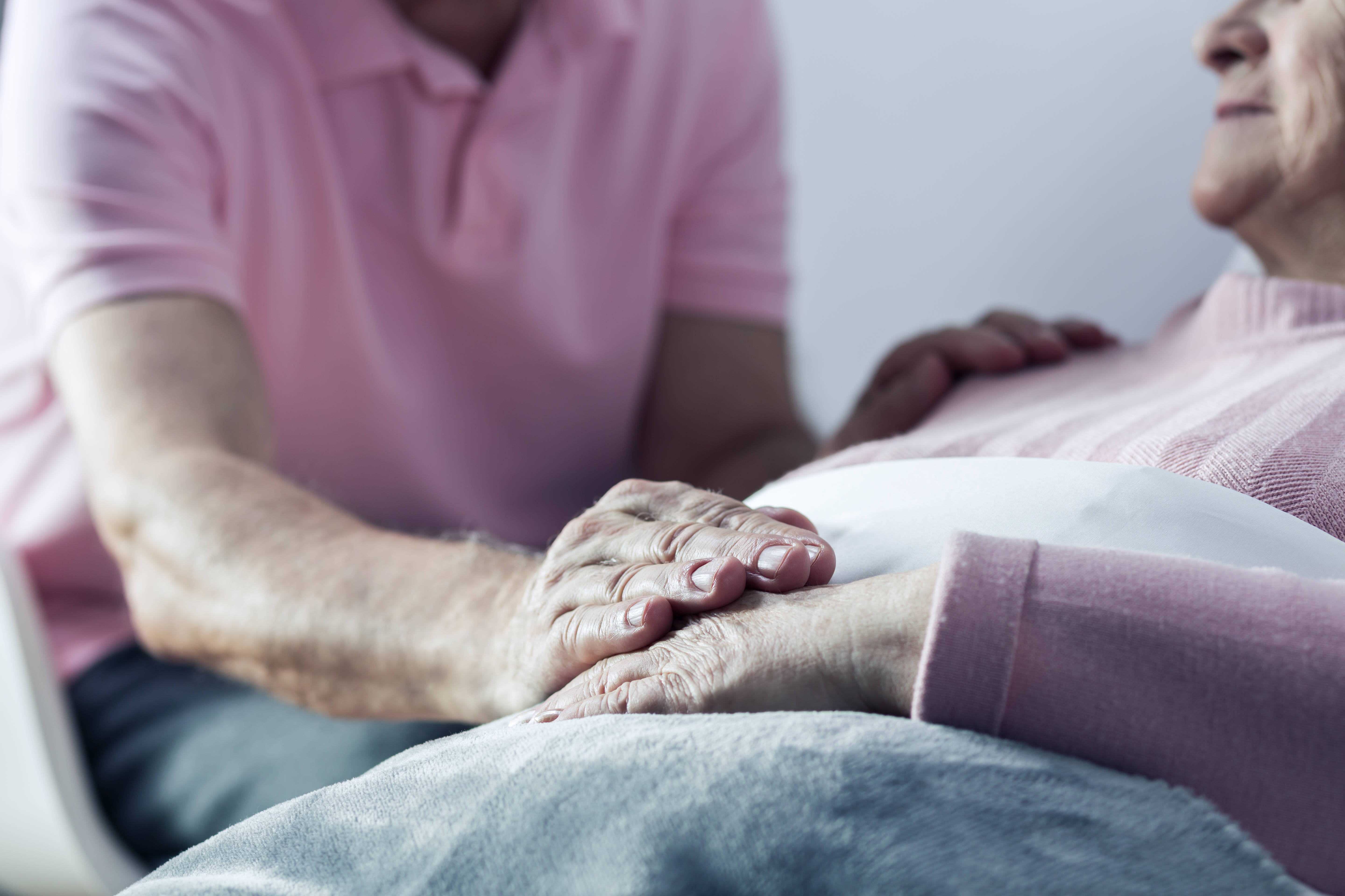 man touching the hand of older person lying in bed