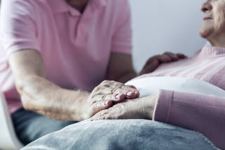 man touching the hand of older person lying in bed