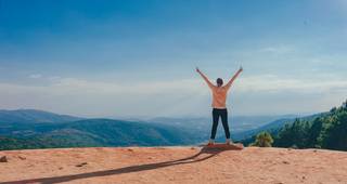 woman standing on cliff edge with arms up